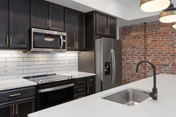 a kitchen with black cabinets and a brick wall at The Madison in Ohio 43215
